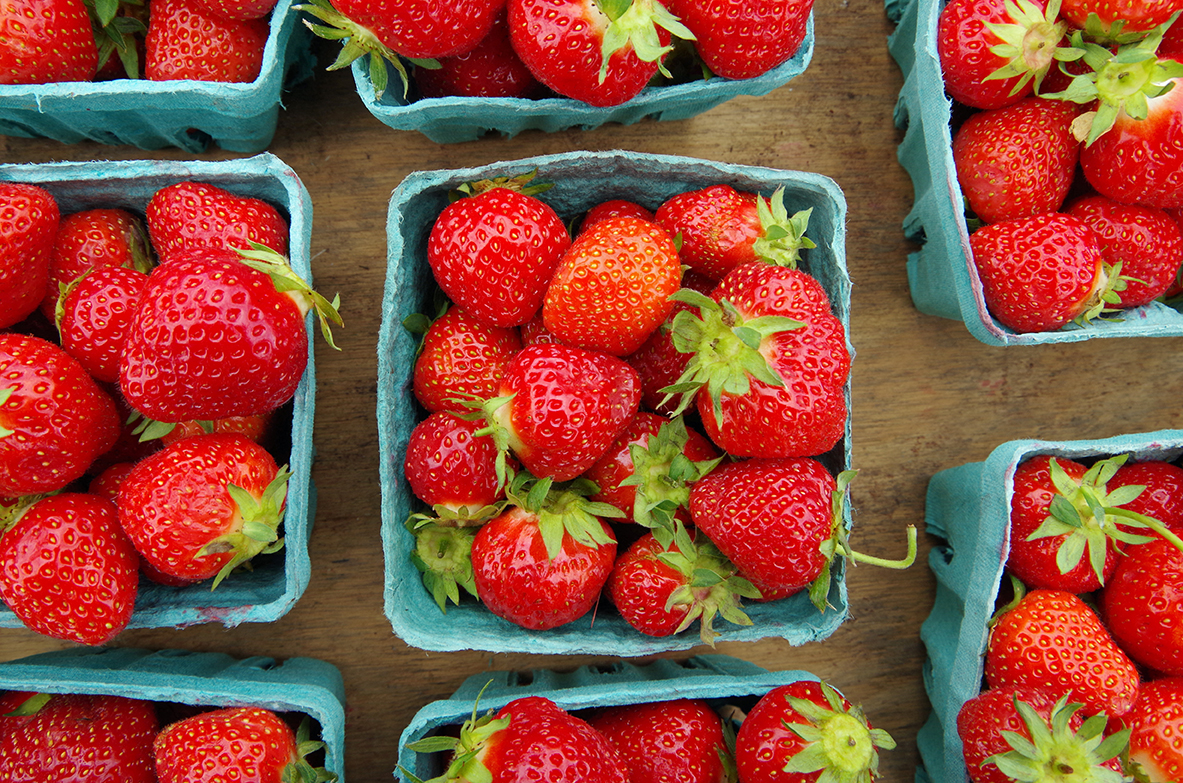 Strawberries, requiring temperature-controlled shipping, sit in baskets on wooden table