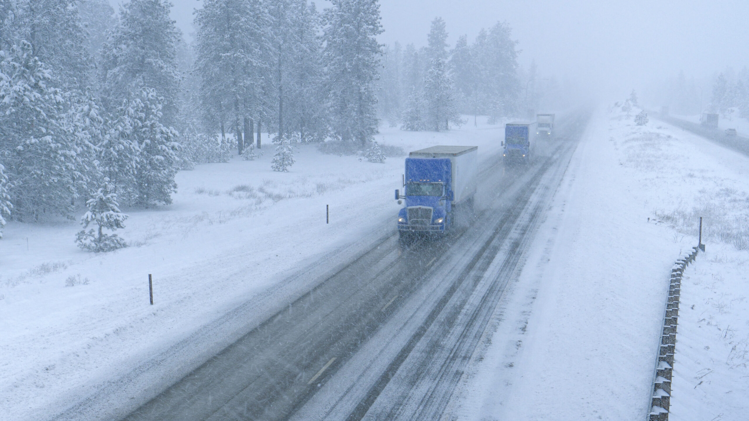Trucks haul containers on road through a snowstorm.